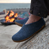 Person wearing blue slippers on a beach with a fire pit in the background
