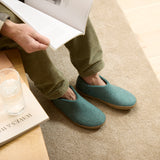 Person wearing North Sea slippers sitting on a couch with a glass of water and book.