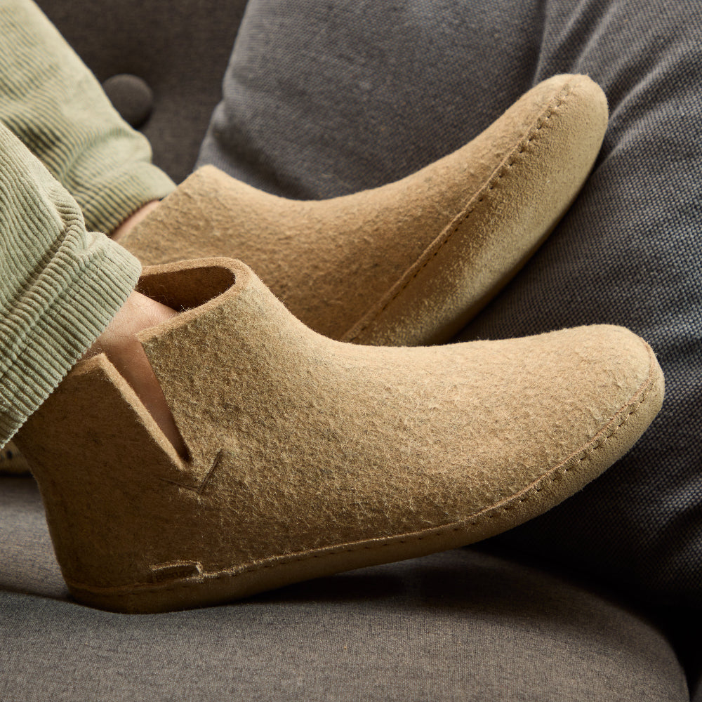 Close-up of beige felt boots worn by a person sitting on a gray couch.