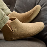 Close-up of beige felt boots worn by a person sitting on a gray couch.