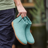 Person holding a pair of teal slippers with a blurred background