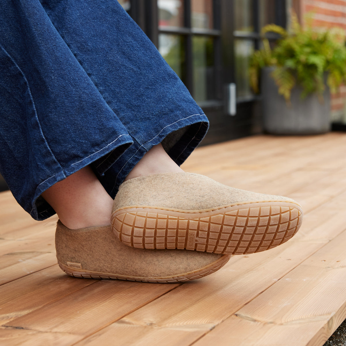 Person wearing sand slippers with honey rubber soles on a wooden deck.