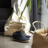 Gold bag, black slippers, and woven basket on a surface near a window.
