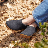 Person wearing dark gray shoes with honey rubber soles on a wooden surface