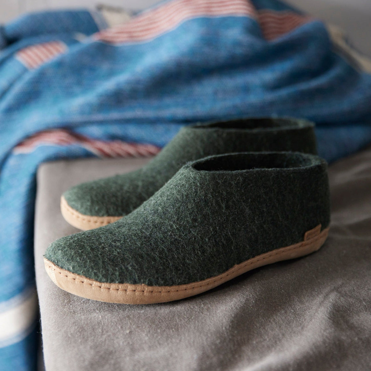 Green slippers on a gray surface with a blue patterned blanket in the background