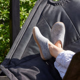 Person relaxing in a gray hammock with feet up, surrounded by greenery.