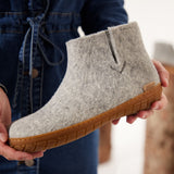 Person holding a gray ankle boot with honey rubber sole