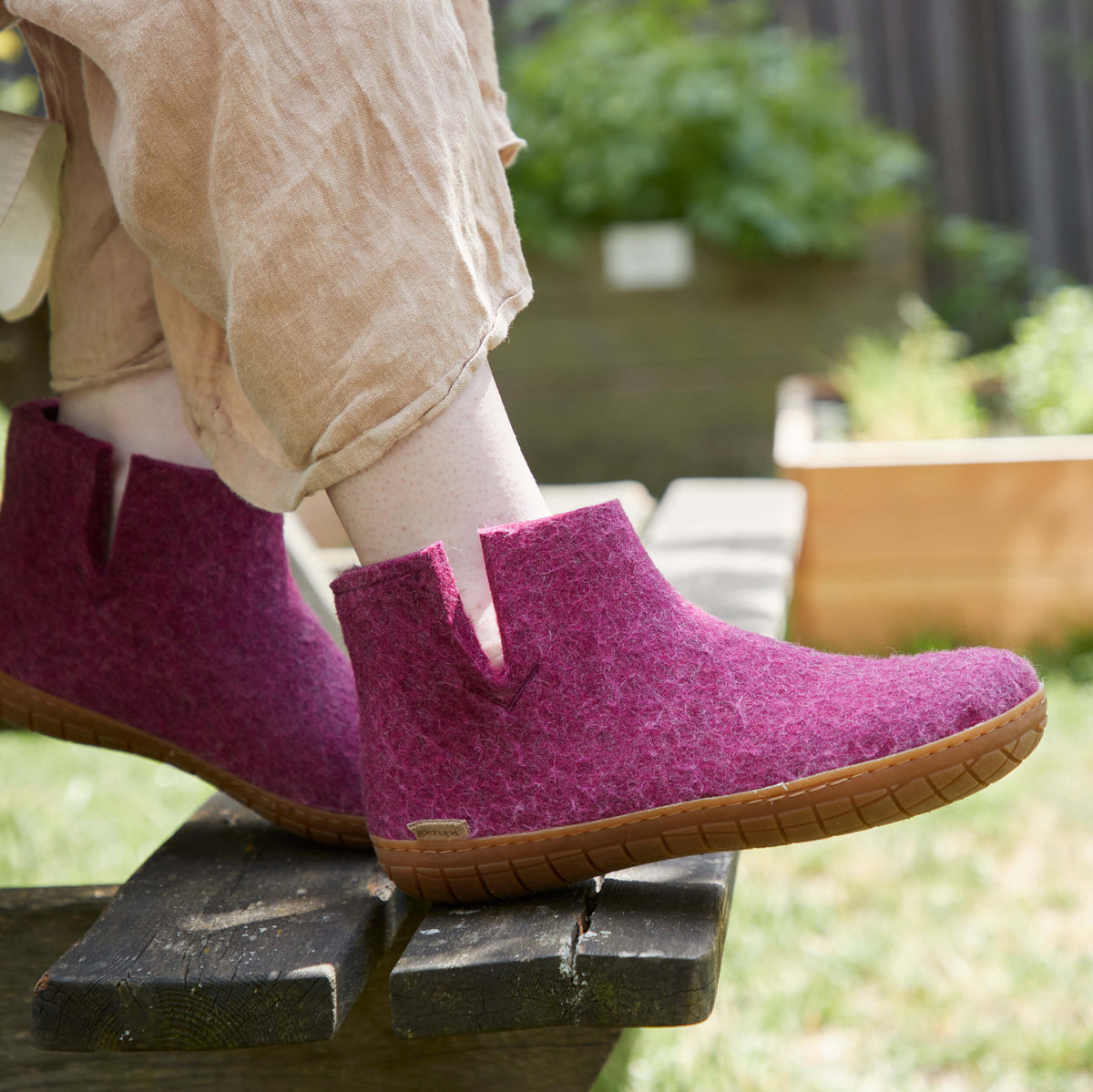 Cranberry boots with honey rubber soles worn by a person sitting outdoors.