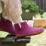 Cranberry boots with honey rubber soles worn by a person sitting outdoors.