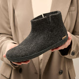 Person holding a gray ankle boot against a beige coat background