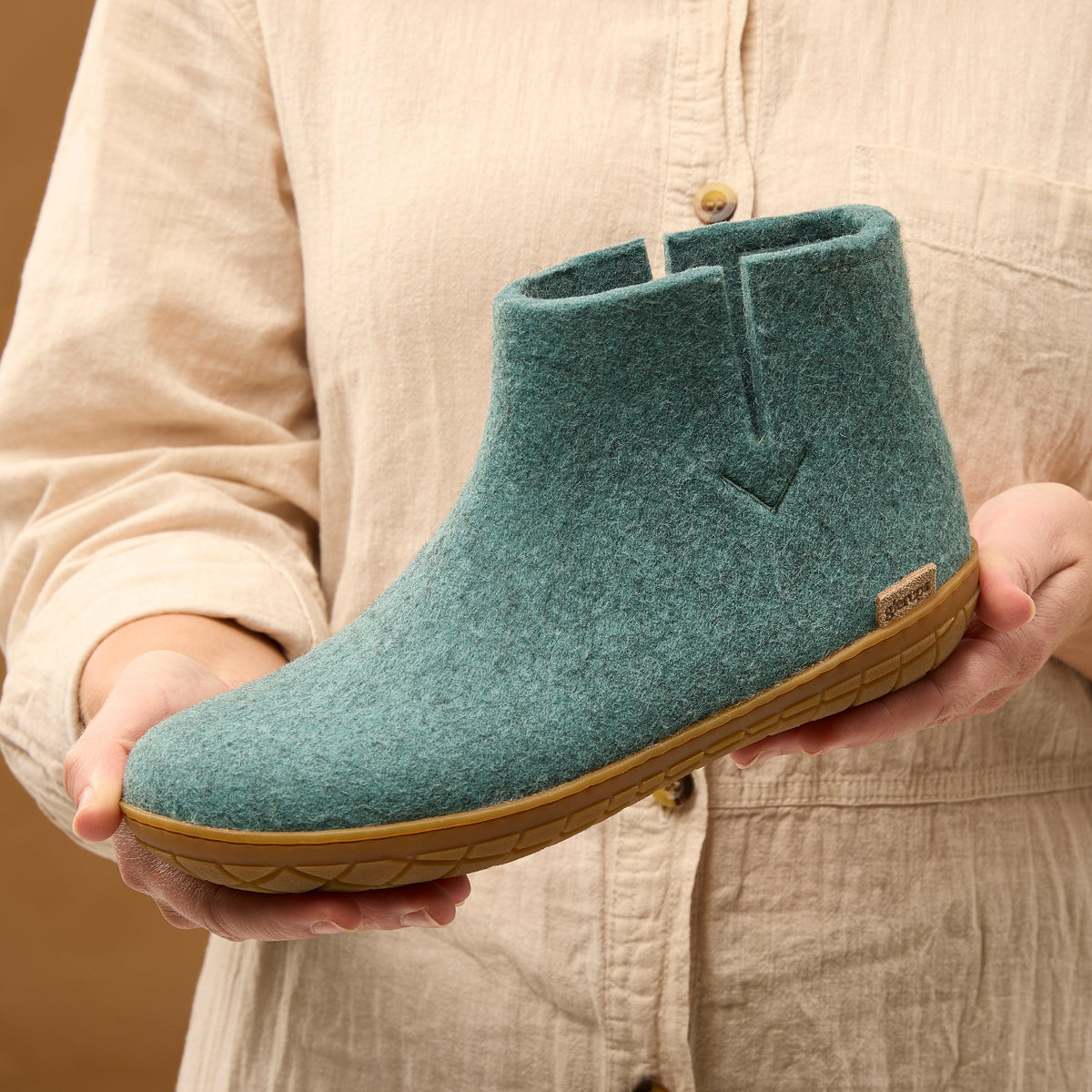 Person holding a teal ankle boot with a honey rubber  sole