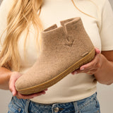 Person holding a brown ankle boot with a honey rubber  sole against a neutral background