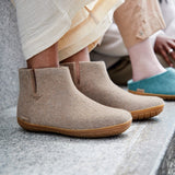 Beige ankle boots with honey rubber  soles worn by a person sitting on a stone surface.