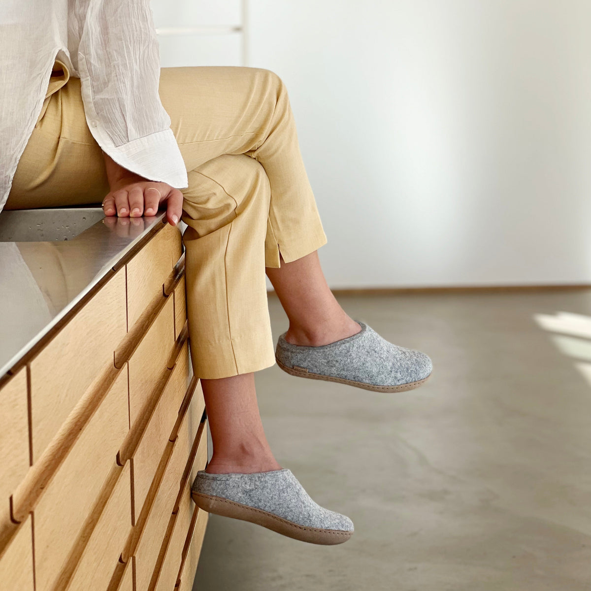 Person wearing gray slippers sitting on a wooden dresser.
