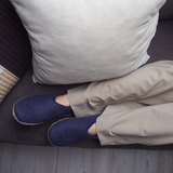 Person wearing blue slippers on a couch with beige pants.