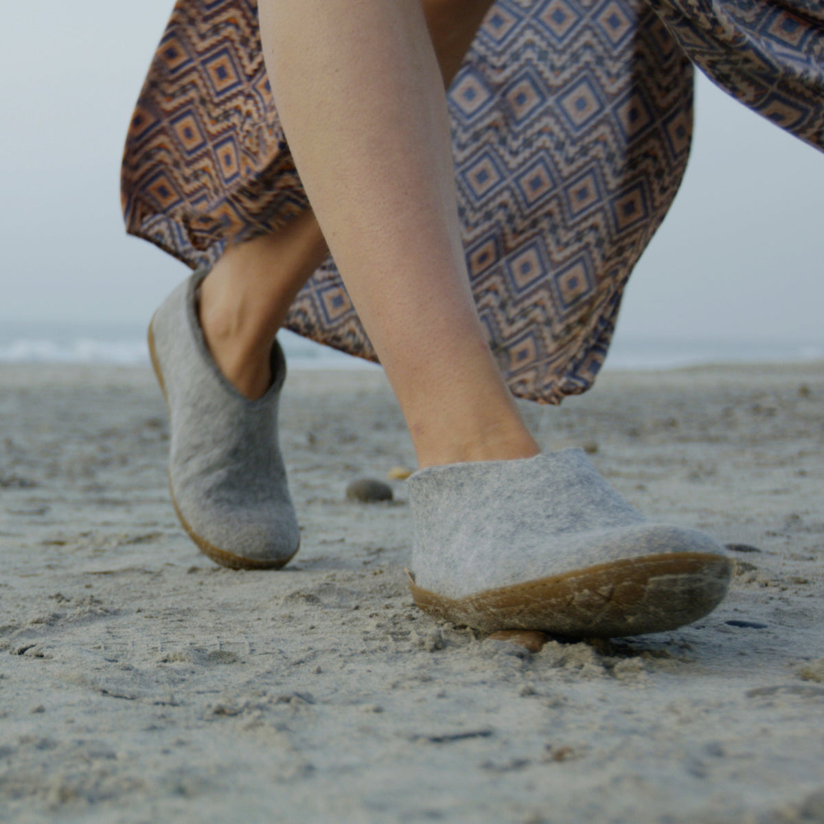 Person wearing gray slippers walking on a sandy beach