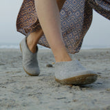 Person wearing gray slippers walking on a sandy beach